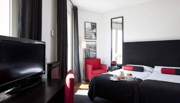 Ein Hotelzimmer mit Bett, Fernseher, einem roten Sessel und einem Esstisch mit Frühstücksangeboten.