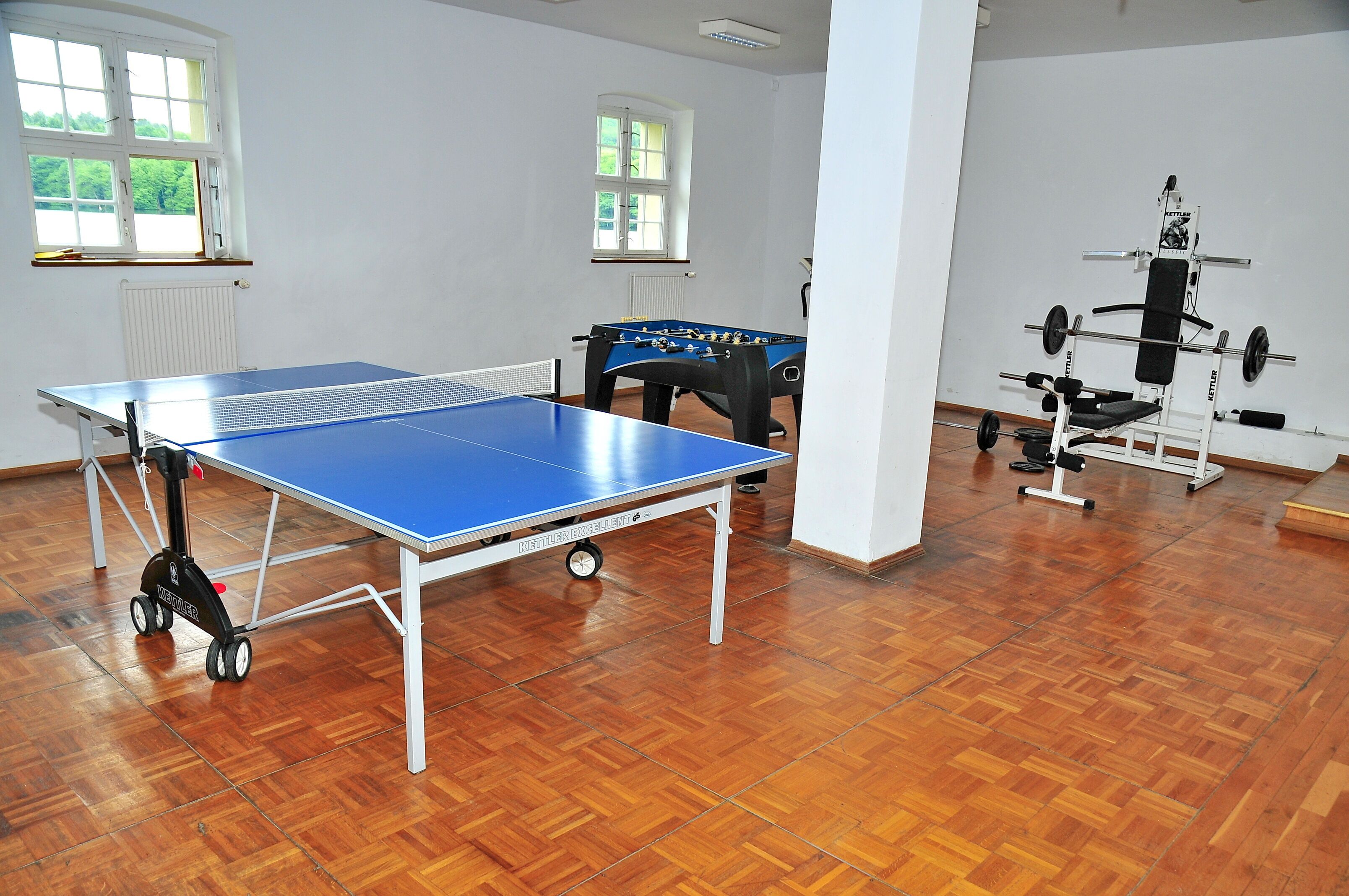 A room with a ping pong table, a foosball table, and a weightlifting station.