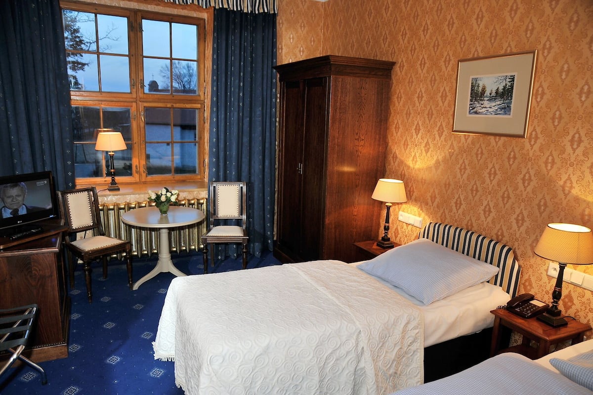 Quarto de hotel com duas camas, uma mesa de trabalho com cadeira, televisão e janela com cortinas.