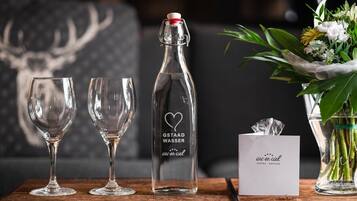 Two empty wine glasses, a bottle of water, a card, and a vase with flowers on a wooden surface.