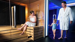 A sauna with wooden benches, a glass partition, and a blue-lit room. - Arc-en-Ciel Gstaad (Saanen)