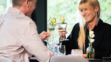 Un homme et une femme sont assis à une table, devant laquelle s’étend un paysage verdoyant. Ils tiennent chacun un verre dans lequel flottent des rondelles de citron vert.