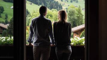 A couple standing by a window overlooking a green landscape with buildings in the distance.