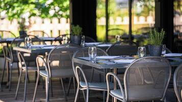 An outdoor dining area with metal tables and chairs, potted plants, and clear glassware.