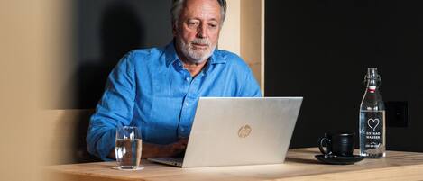 A man sitting at a wooden table with a laptop, a glass of water, and a bottle of water.