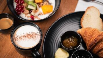 Ein Frühstückstisch mit einer Schüssel Müsli, einem Croissant und einer Tasse Kaffee.