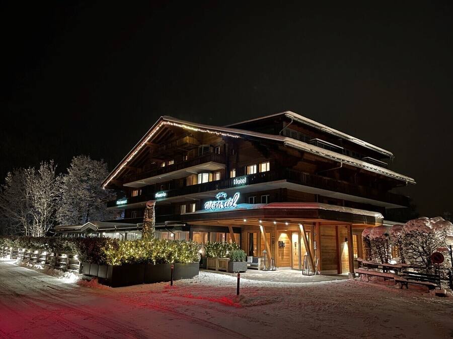 Een meerlaags hotel met een bord voor een skigebied, houten gevel en verlichte entree.