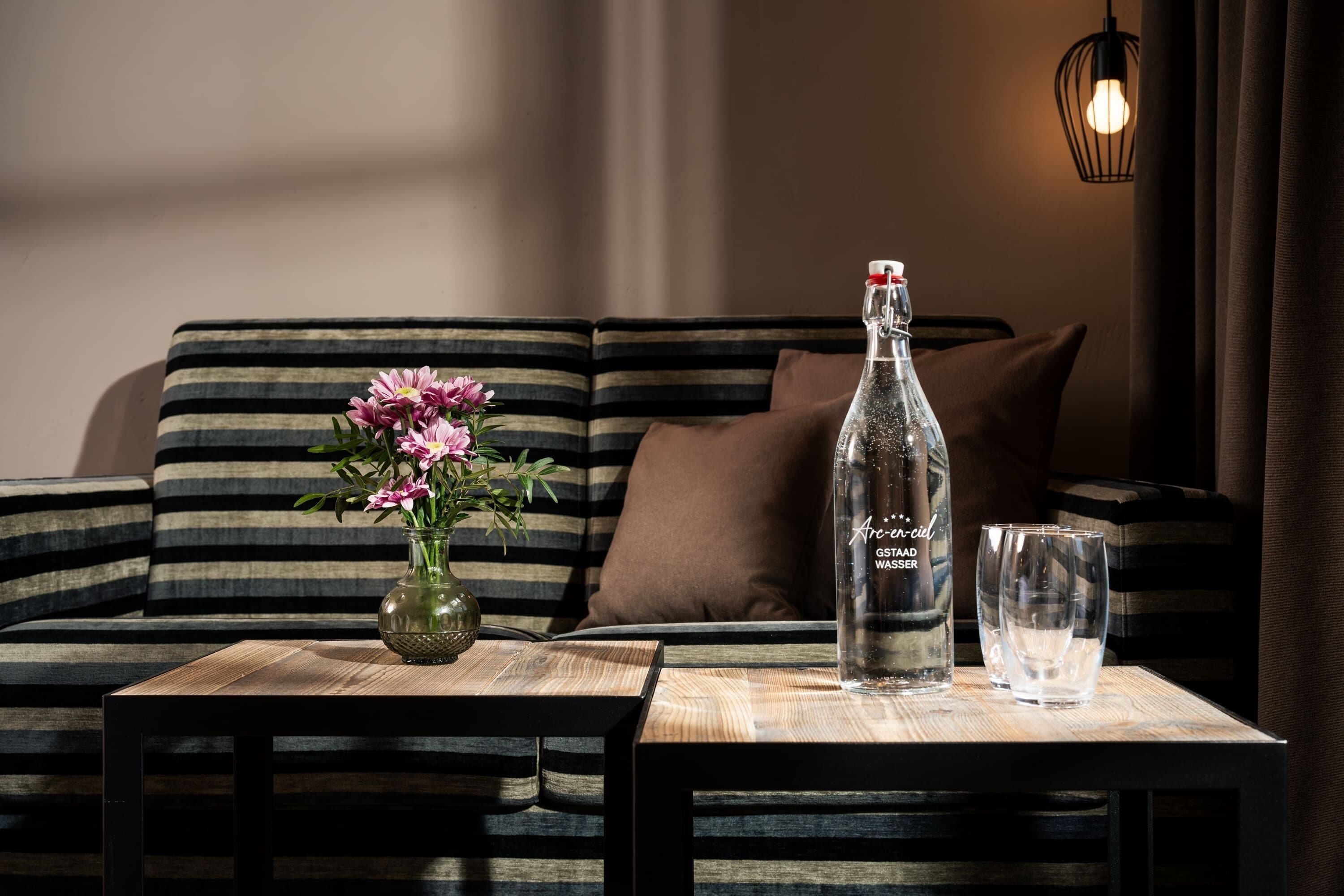 A wooden table with a bottle of water, a vase with flowers, and a glass on a striped sofa.