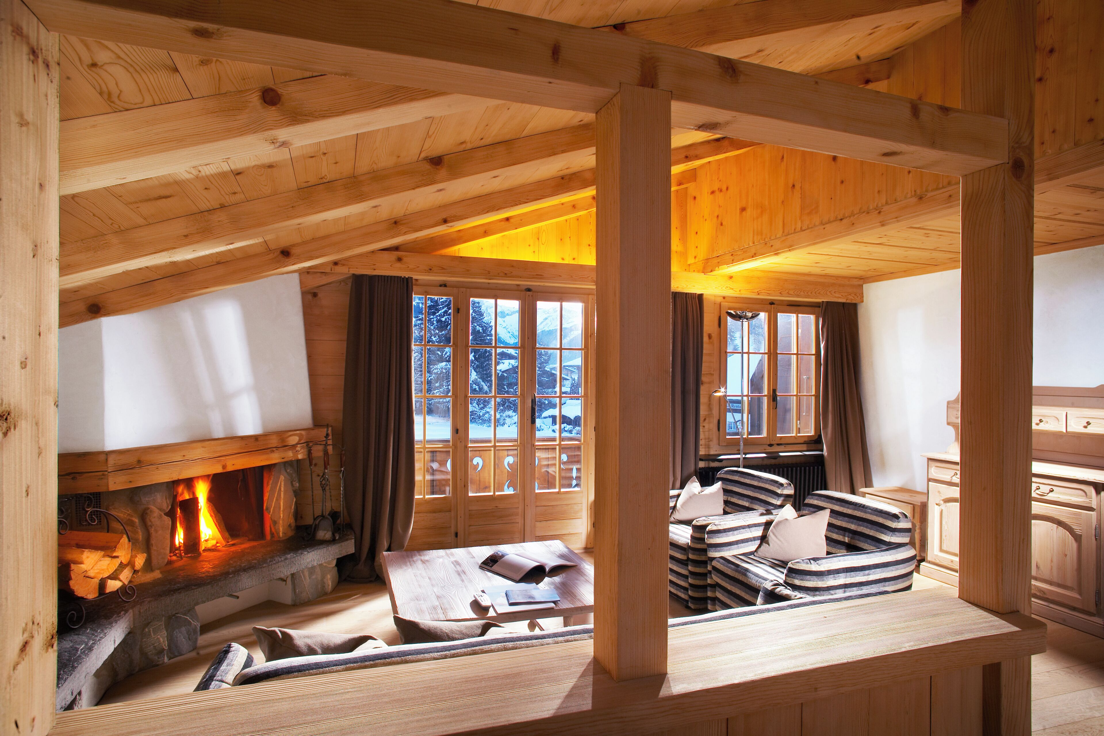 Acogedor interior de cabaña de troncos con chimenea, muebles de madera y ventanas amplias.