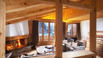 A cozy log cabin interior with a fireplace, wooden furniture, and large windows.