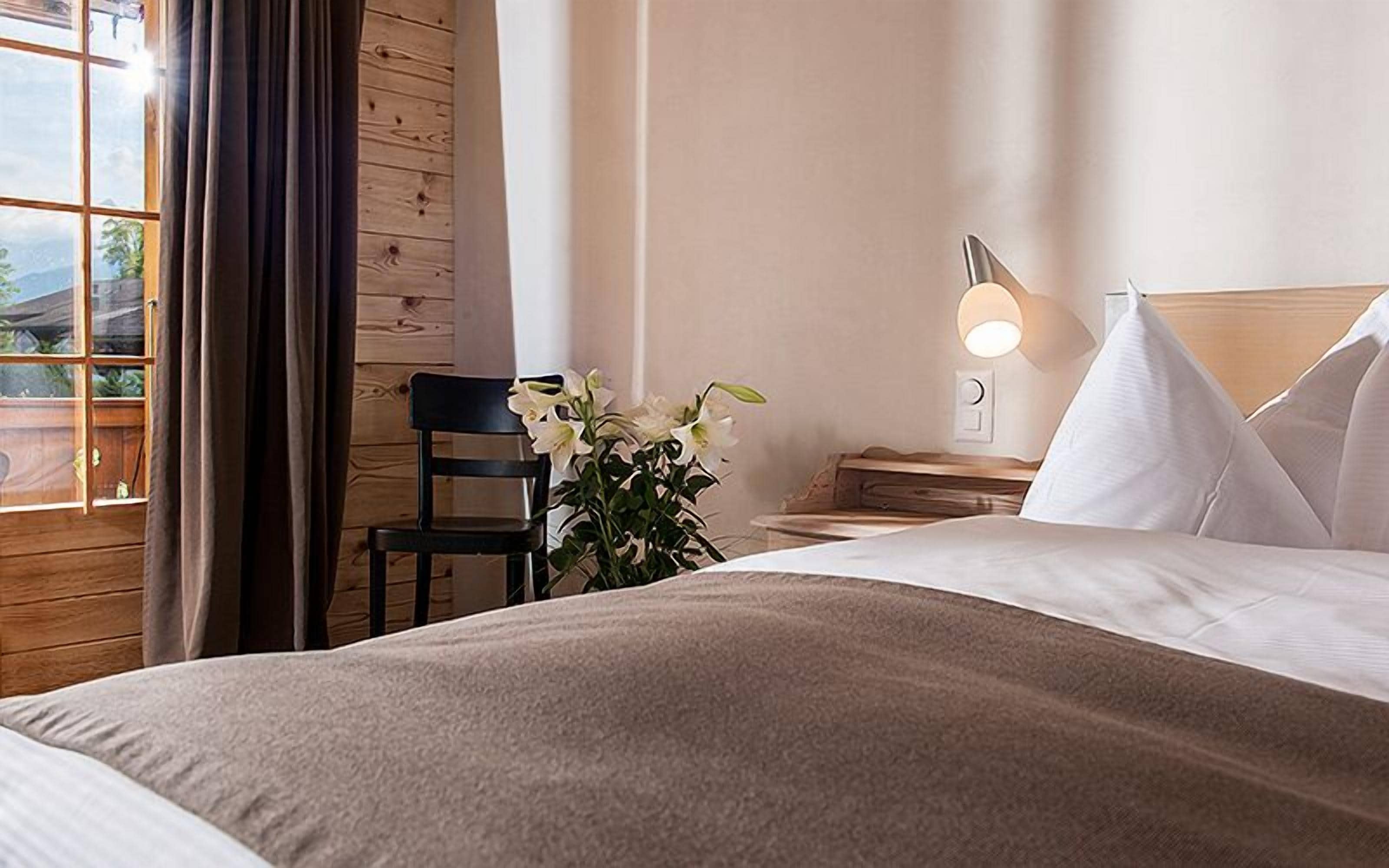 Ein Hotelzimmer mit Bett, Nachttisch mit Lampe, Stuhl und Blumen in einer Vase.