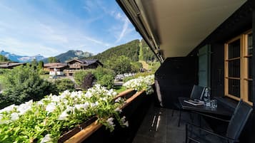 Un balcon avec une table et des chaises, donnant sur un paysage montagneux parsemé de bâtiments et de verdure.