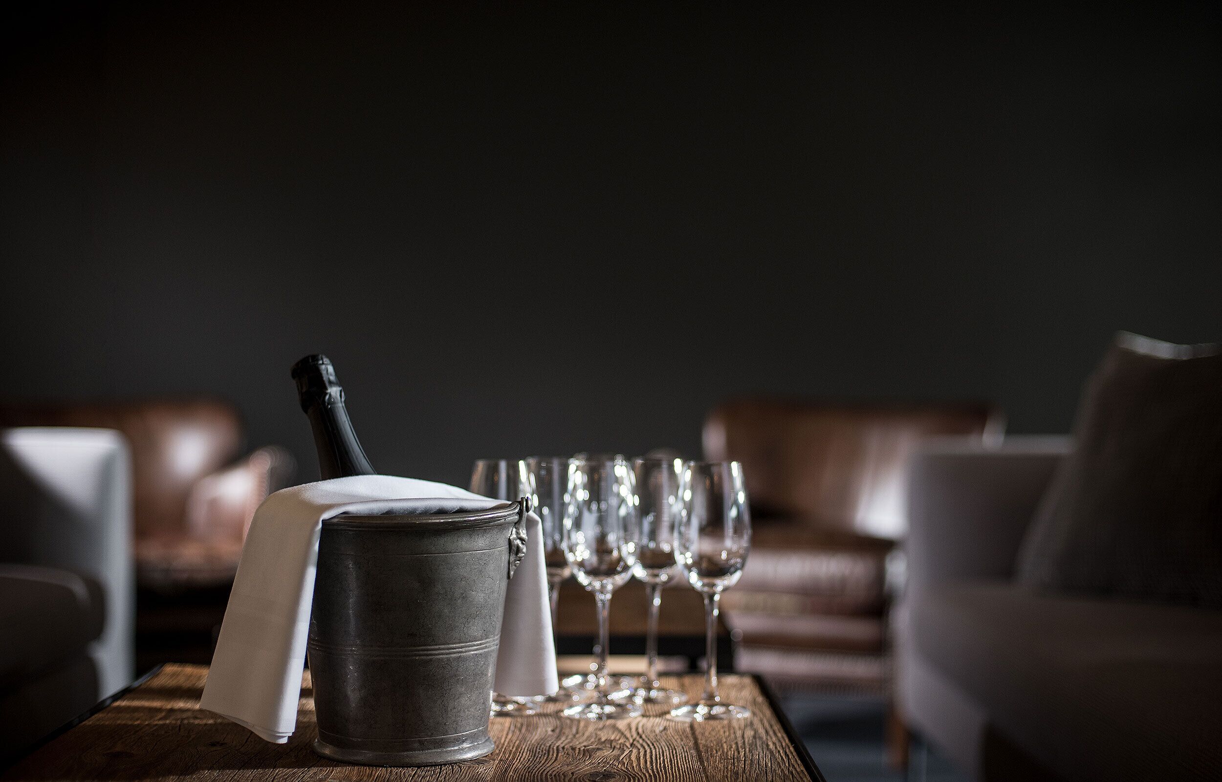 Une table en bois, sur laquelle se trouvent un seau en métal et une bouteille, entourée de verres à vin vides.