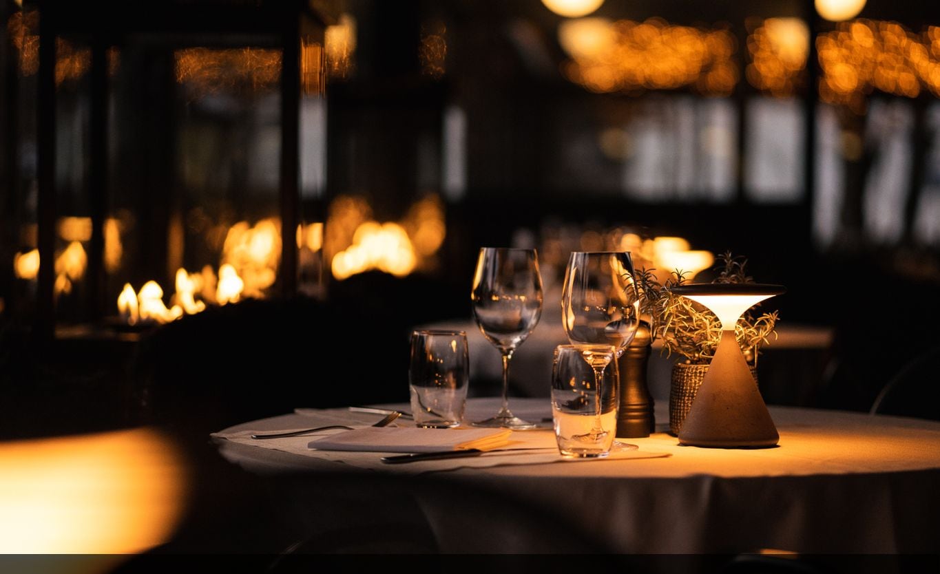 Une scène de restaurant avec une table dressée pour le dîner, comprenant des verres à vin et un chandelier servant de décoration centrale.