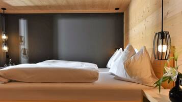 A bedroom with a bed, pillows, a nightstand, a vase with flowers, and a wall-mounted light fixture.