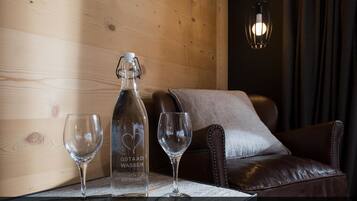 A wooden interior with a leather sofa, a table with a bottle and glasses, and a hanging light fixture.