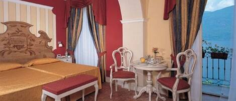 A hotel room with a large bed, two chairs, a small table, and a balcony with a view.