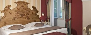 A bed with a decorative headboard, a window with curtains, and a small table.