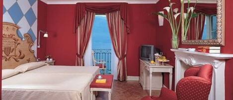 A hotel room with a bed, a desk, a chair, a television, and a view of the sea through the window.