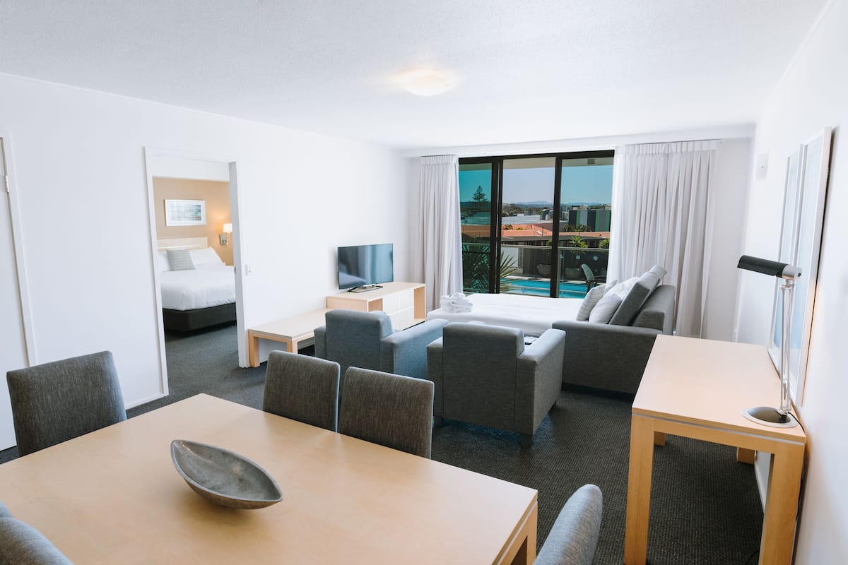Ein Hotelzimmer mit Essbereich, einer Couch, einem Fernseher, einem kleinen Tisch und einem Balkon mit Blick.