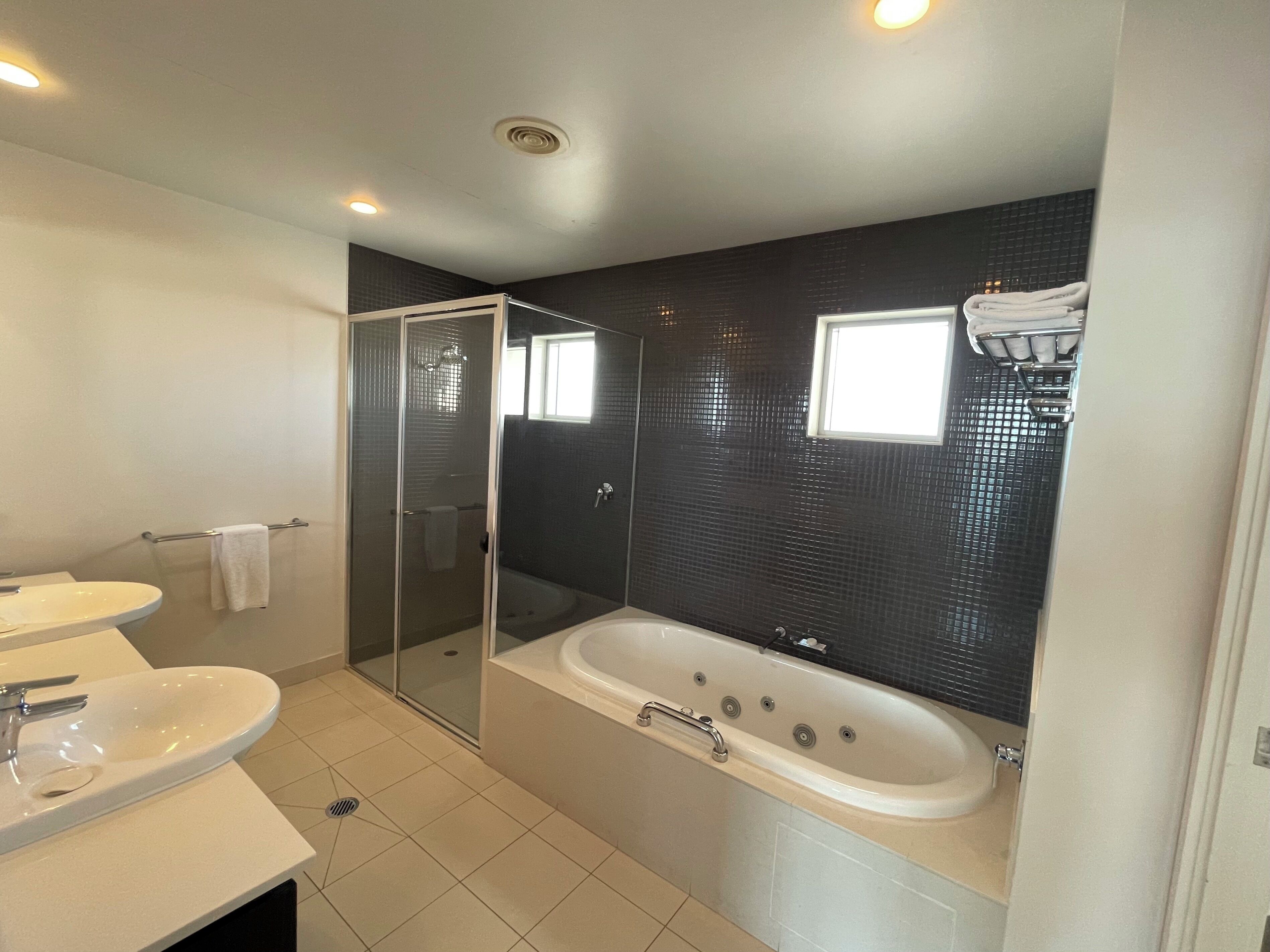 A modern bathroom with a glass-enclosed shower, a large bathtub, and two sinks.