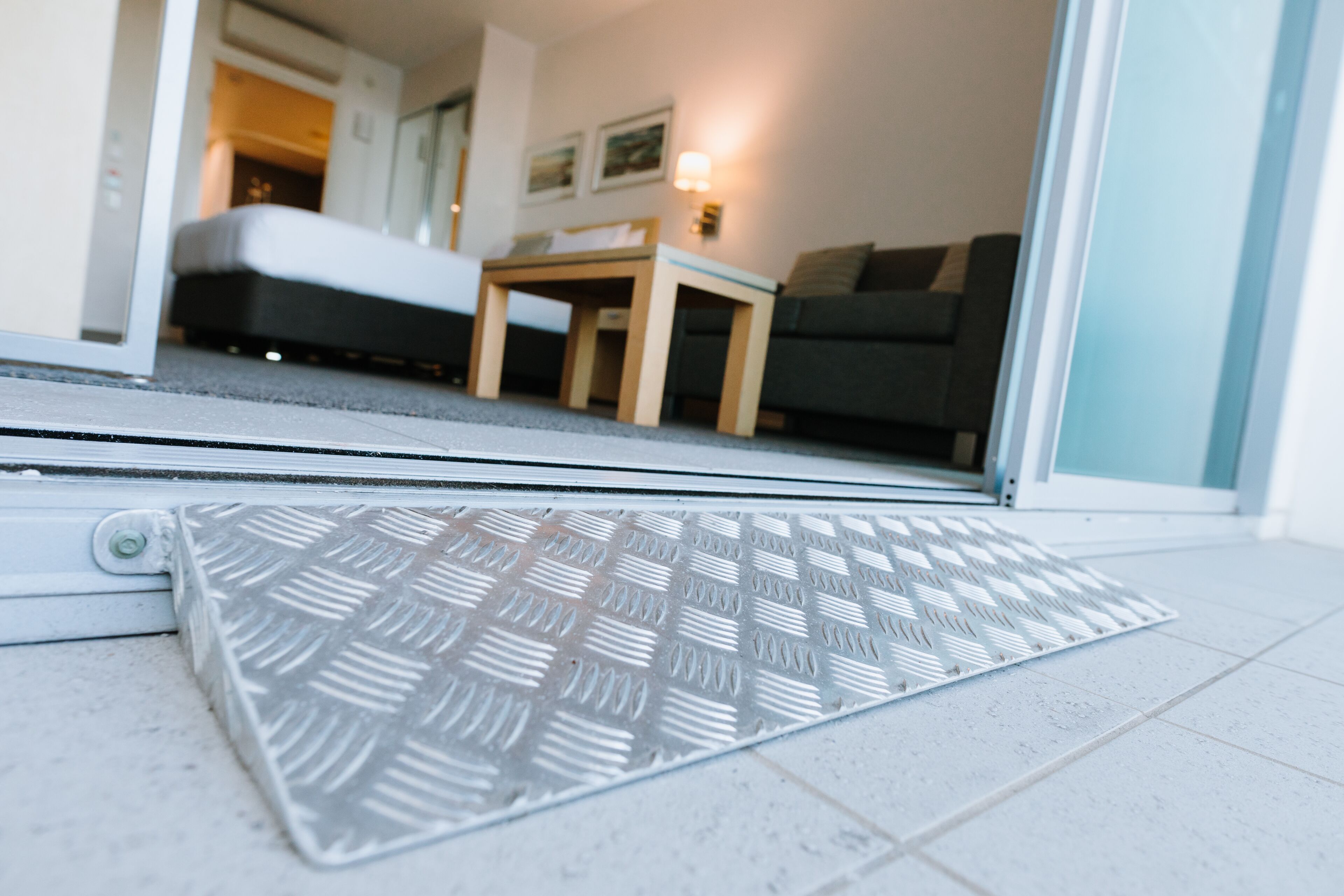 A hotel room entrance with a sliding door, a patterned mat, a bed, a small table, and a sofa.
