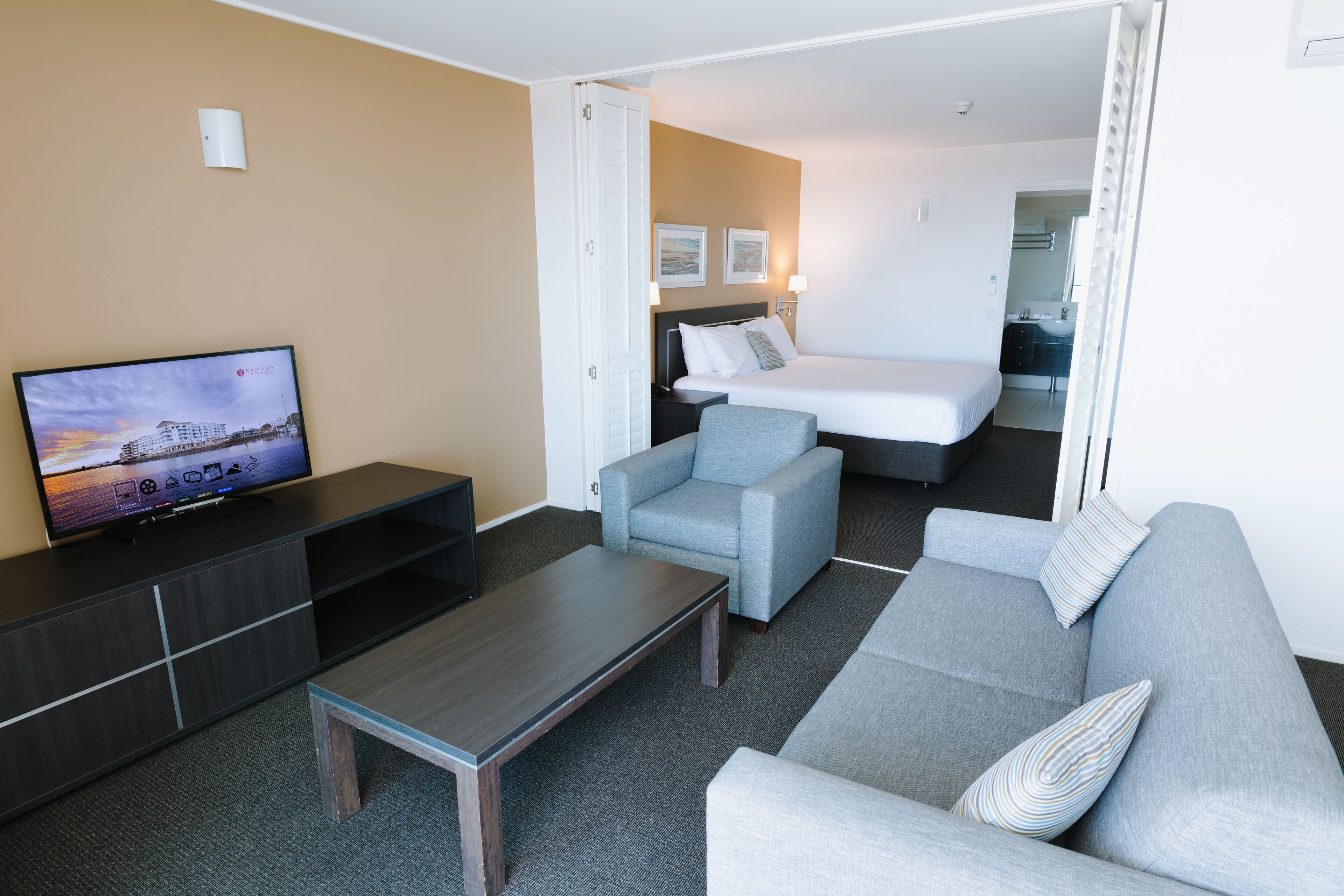 Une chambre d’hôtel moderne équipée d’un téléviseur à écran plat, d’un canapé, d’un fauteuil, d’un lit et d’une petite table.