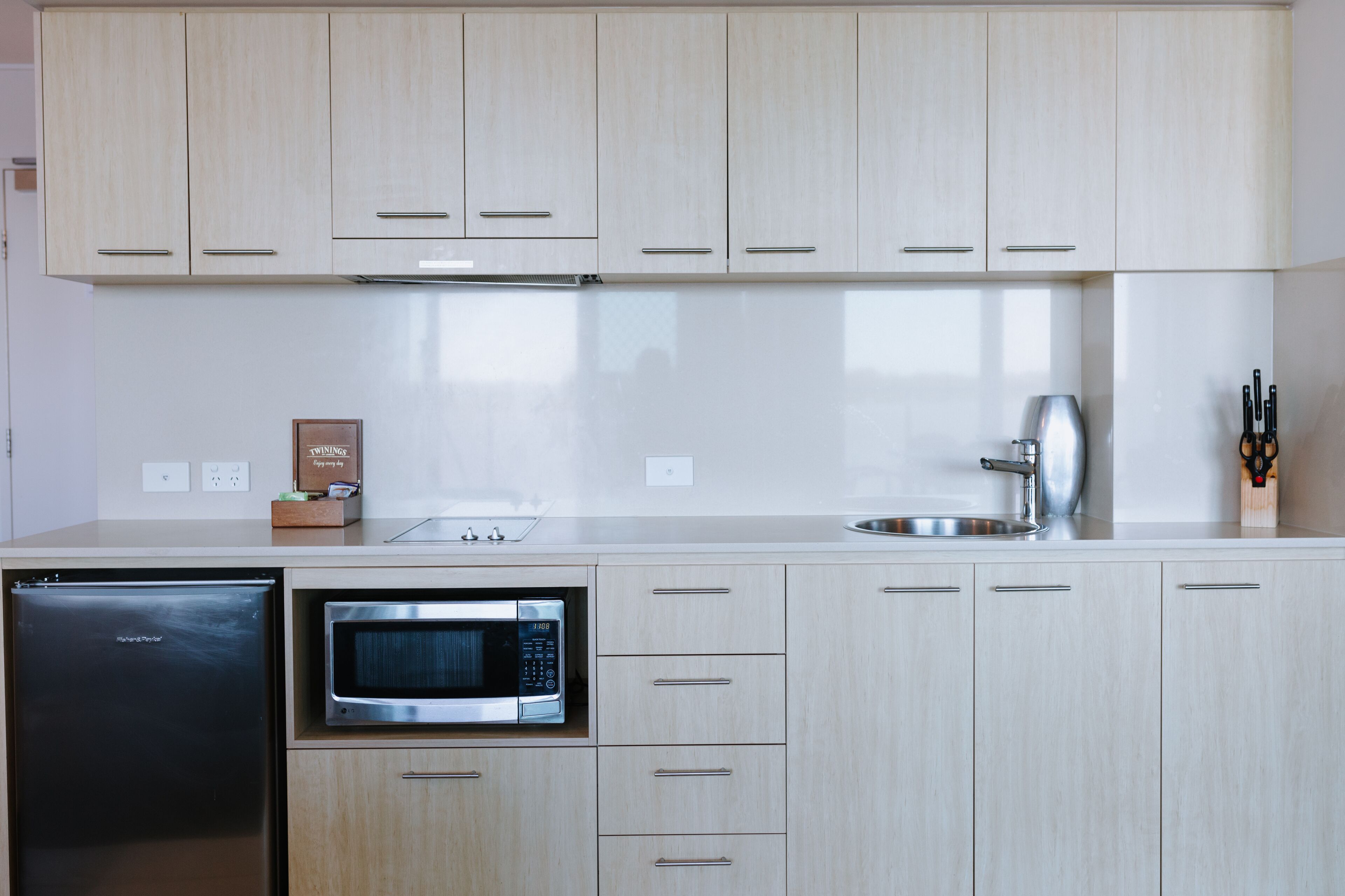 A modern kitchen with light wood cabinets, a stainless steel microwave, and a dishwasher.