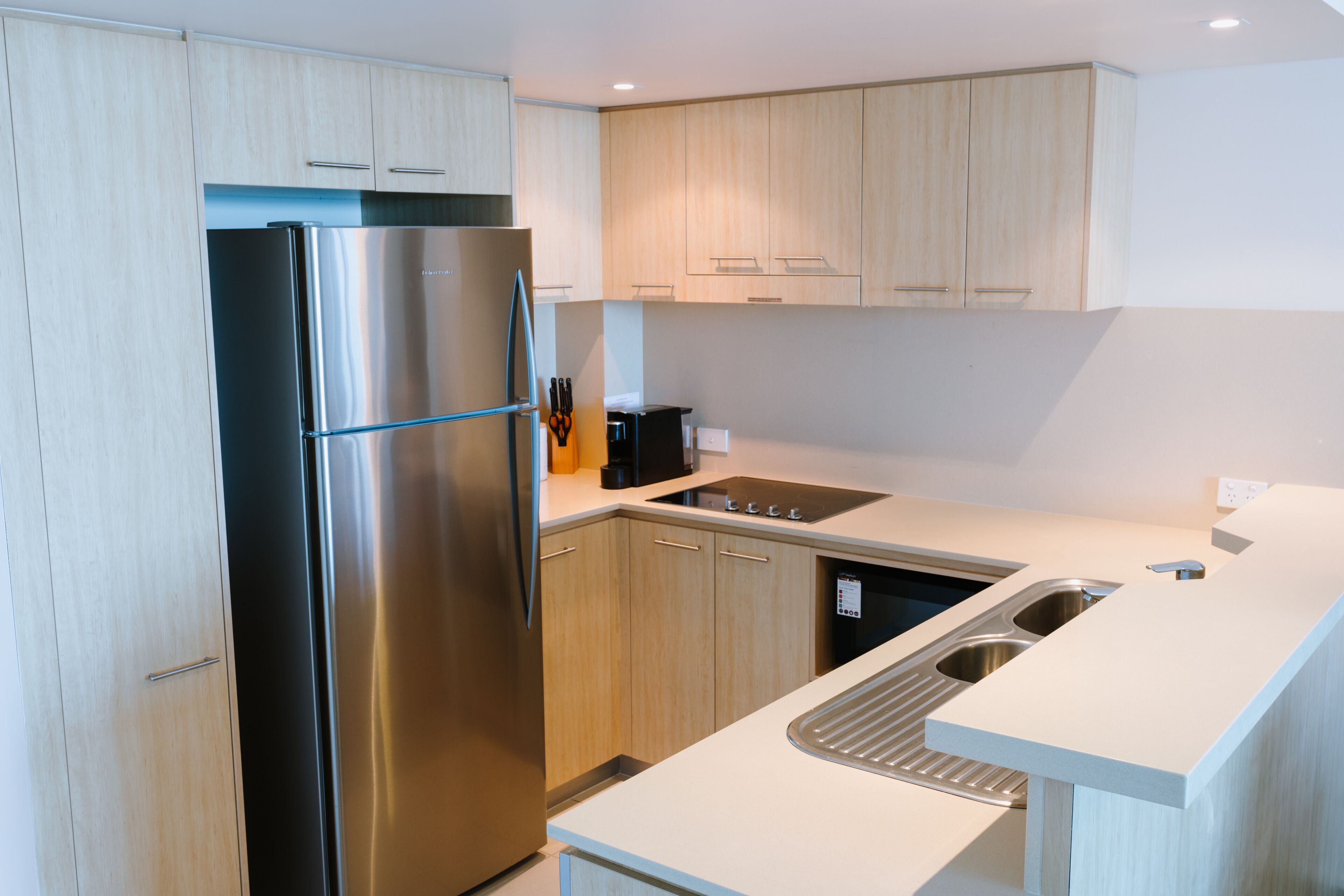 A modern kitchen with light wood cabinets, a stainless steel refrigerator, and a white countertop.