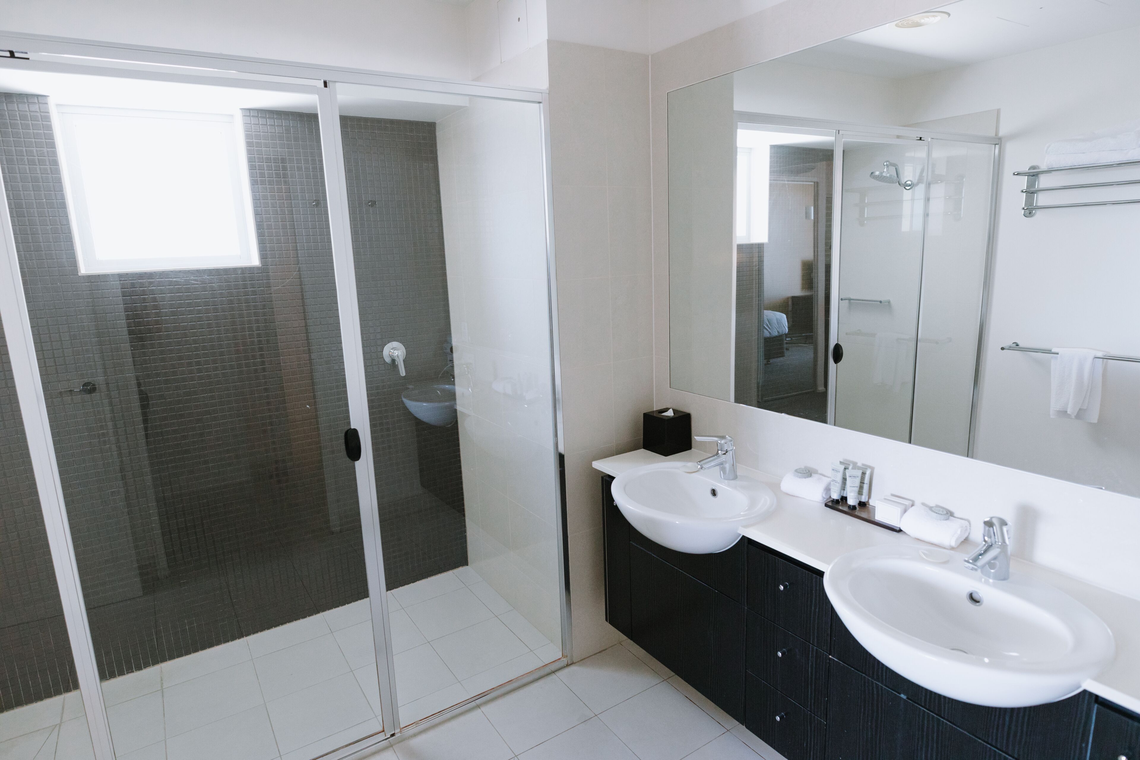 Un baño moderno con dos lavamanos, un espejo grande y una ducha con cerramiento de vidrio.
