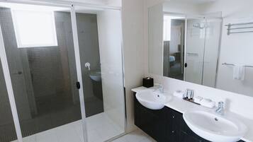 Un baño moderno con dos lavamanos, un espejo grande y una ducha con cerramiento de vidrio.