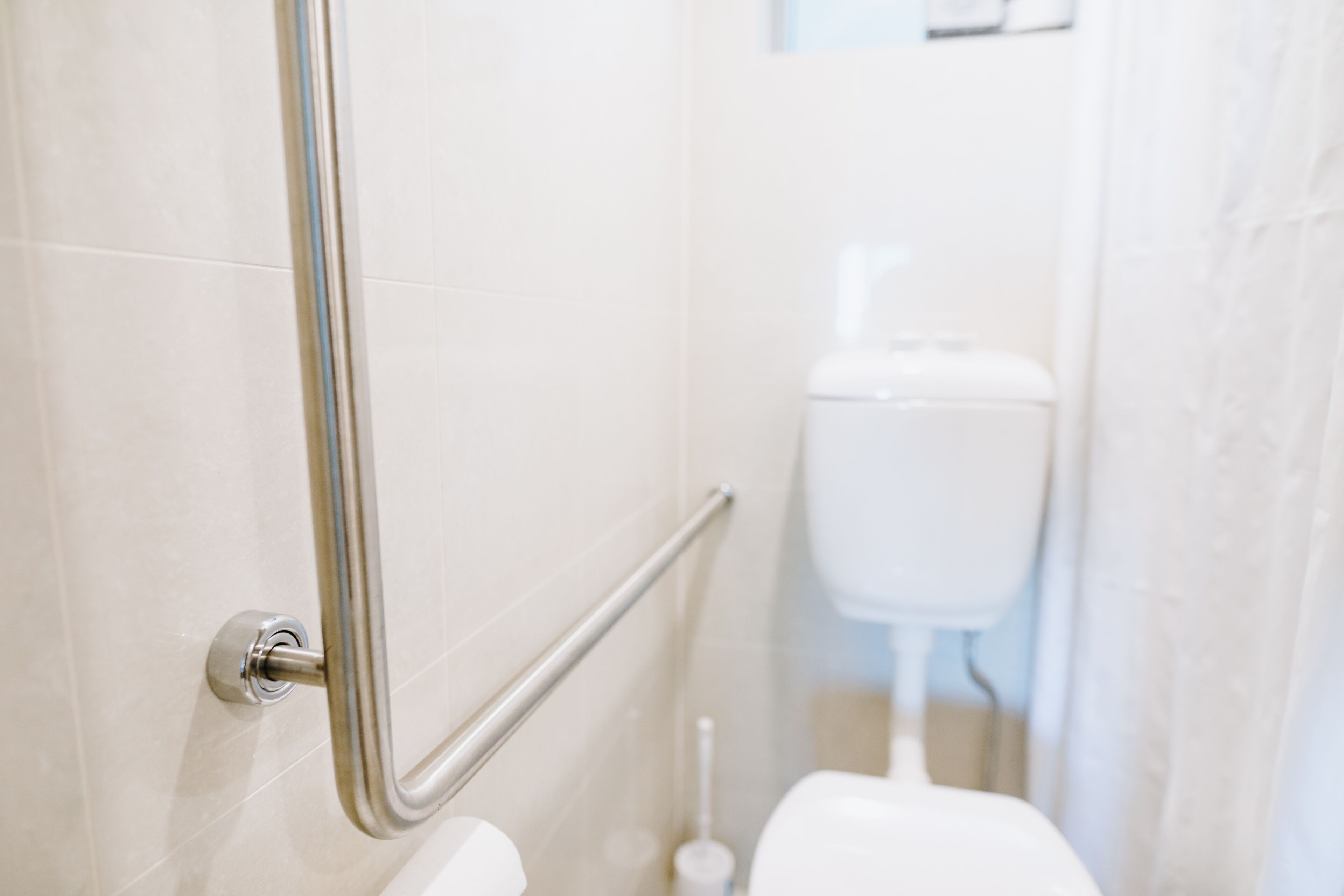 A bathroom with a handrail, a toilet, and a bidet.