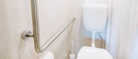 A bathroom with a handrail, a toilet, and a bidet.