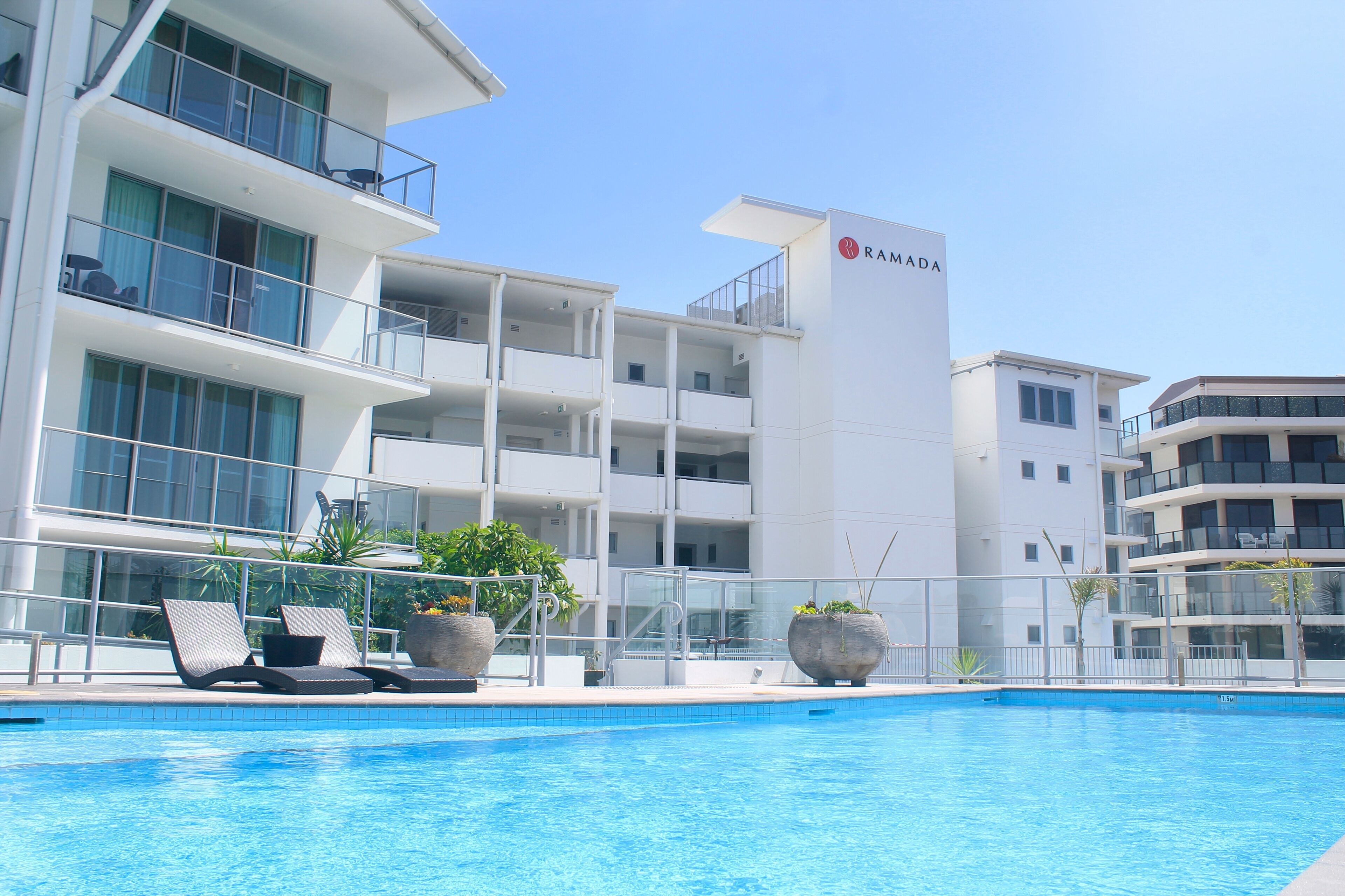 A modern hotel with a swimming pool, lounge chairs, and potted plants.