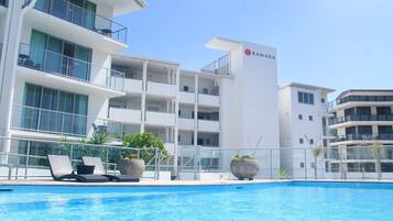 A modern hotel with a swimming pool, lounge chairs, and potted plants.