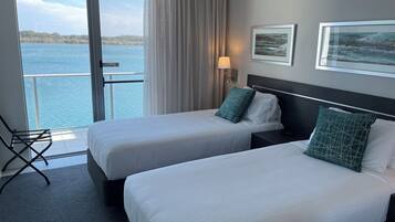 Ein Hotelzimmer mit zwei Betten, Meerblick, einem Sessel und einer Lampe.