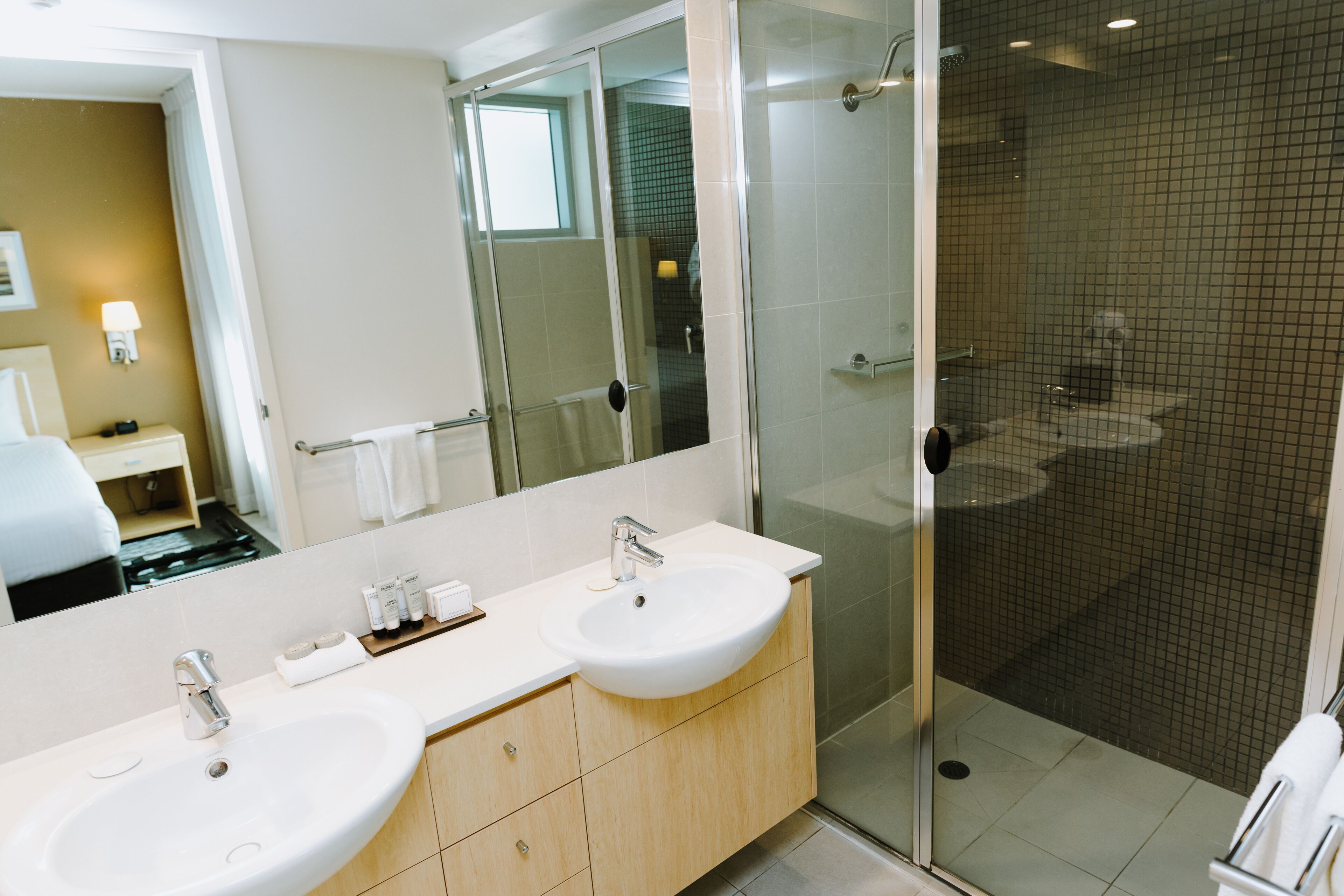 Ein modernes Badezimmer mit zwei Waschbecken, einem großen Spiegel und einer Duschkabine.