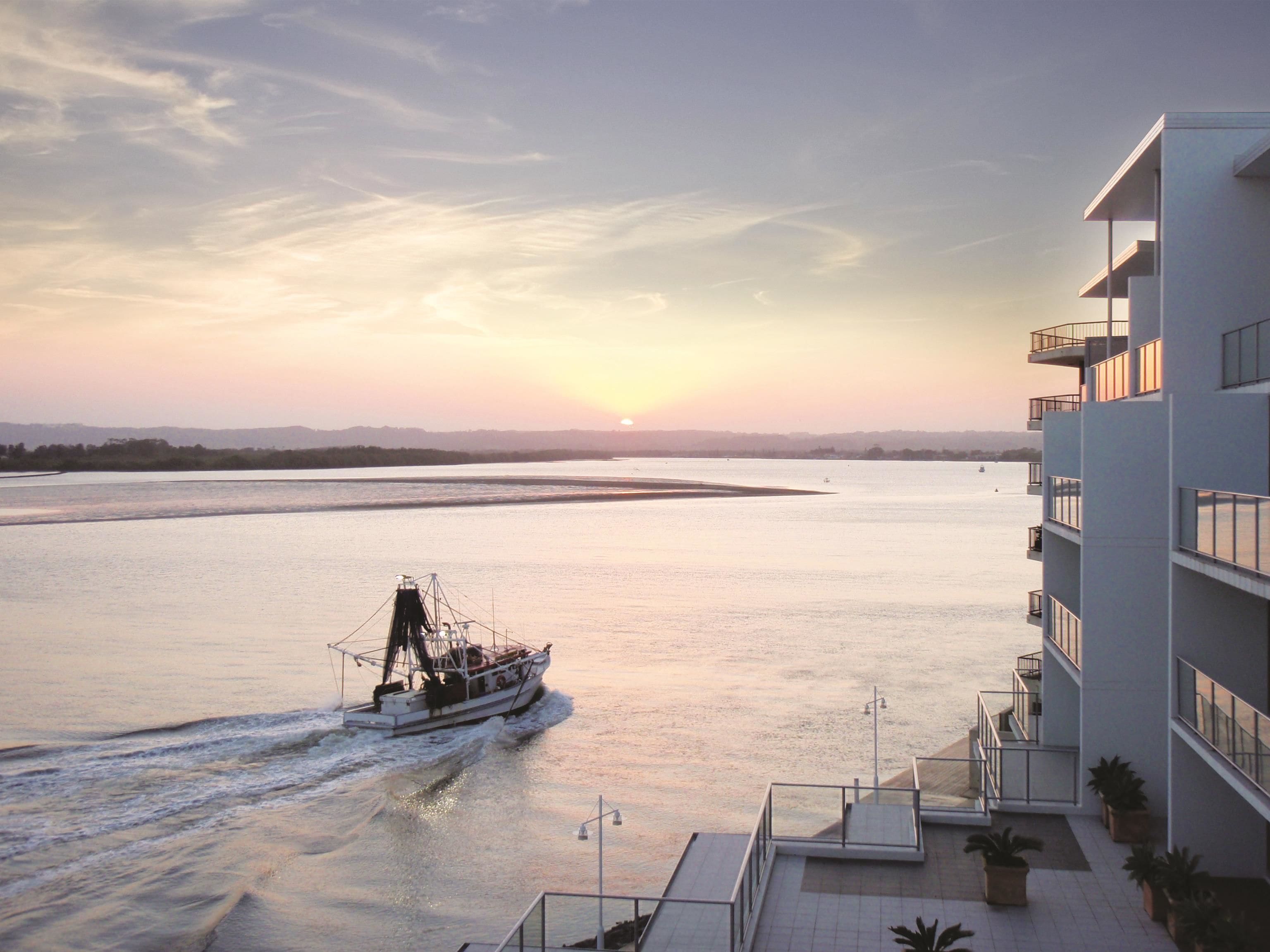 Een boot op een rustige rivier met een modern gebouw aan de rechterkant.