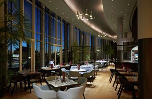 Ein modernes Restaurant mit hohen Decken, großen Fenstern und mehreren Essplätzen.