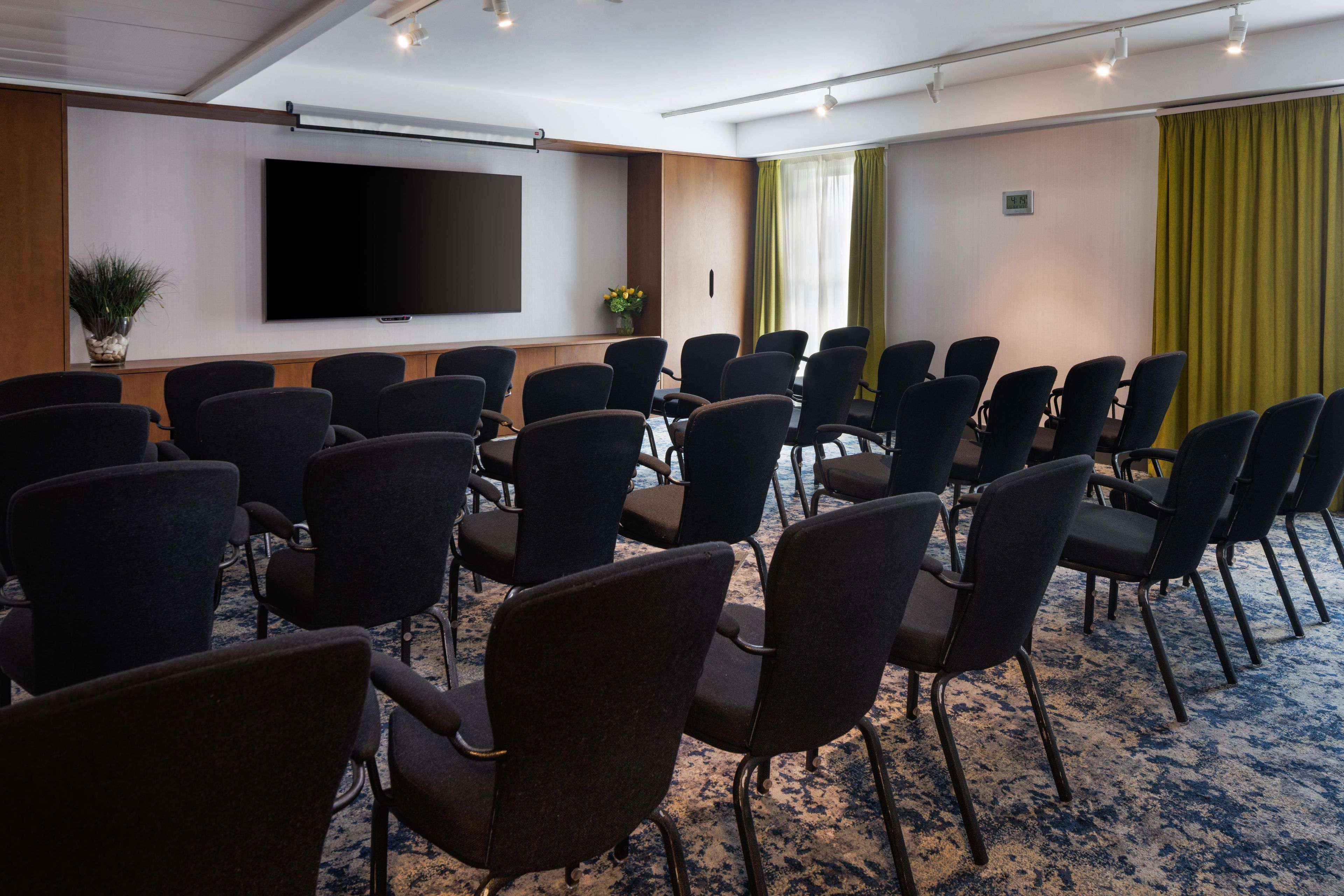 A conference room with rows of chairs, a large flat-screen TV, and a clock on the wall.