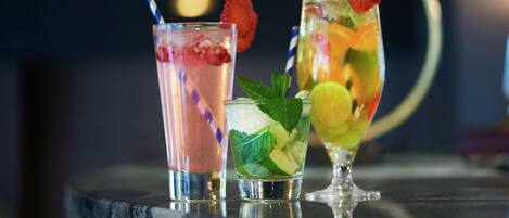 Three cocktails with fruit garnishes on a reflective surface.