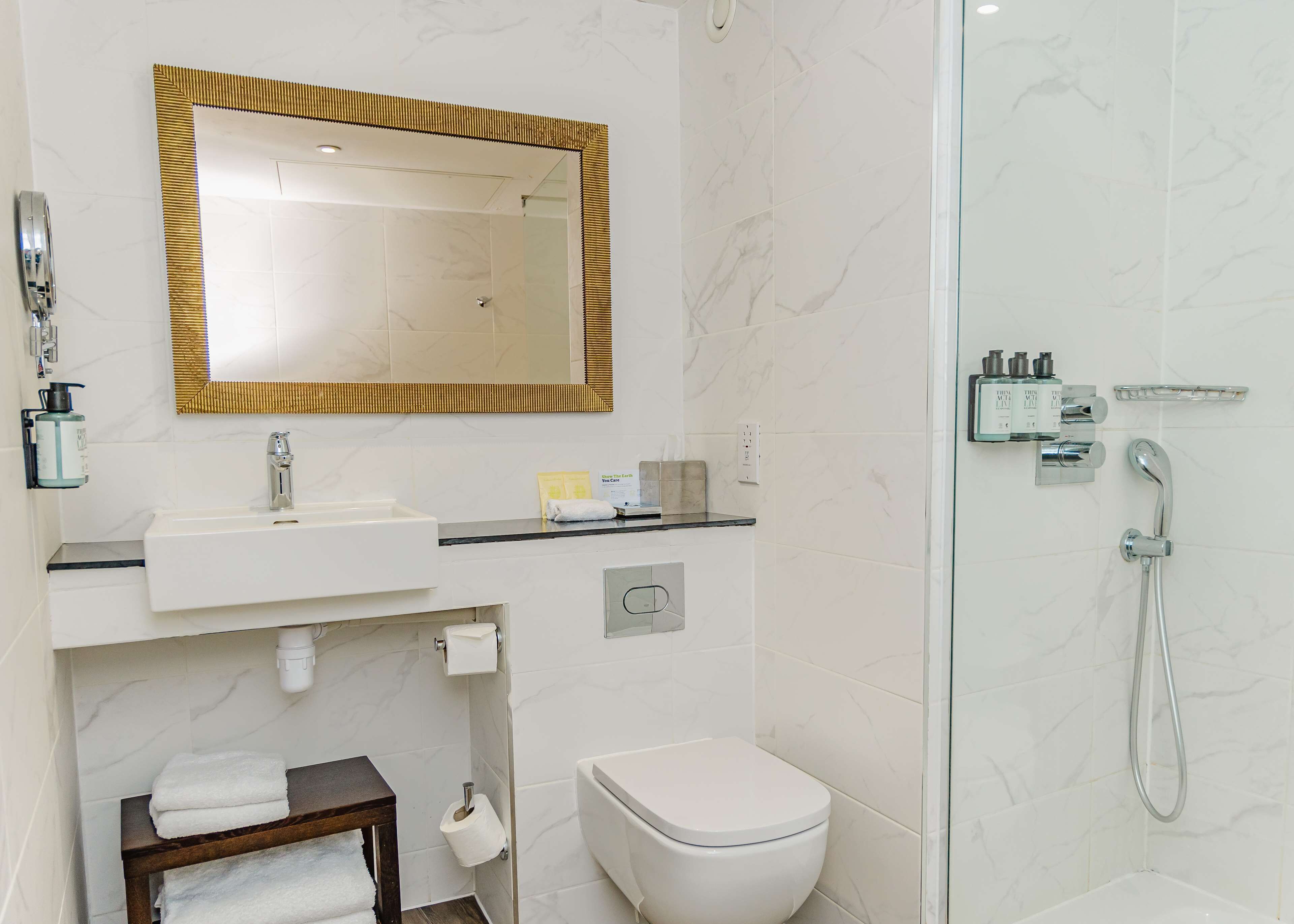 Une salle de bain moderne avec un lavabo blanc, des toilettes, une douche et un miroir doté d’un cadre doré.