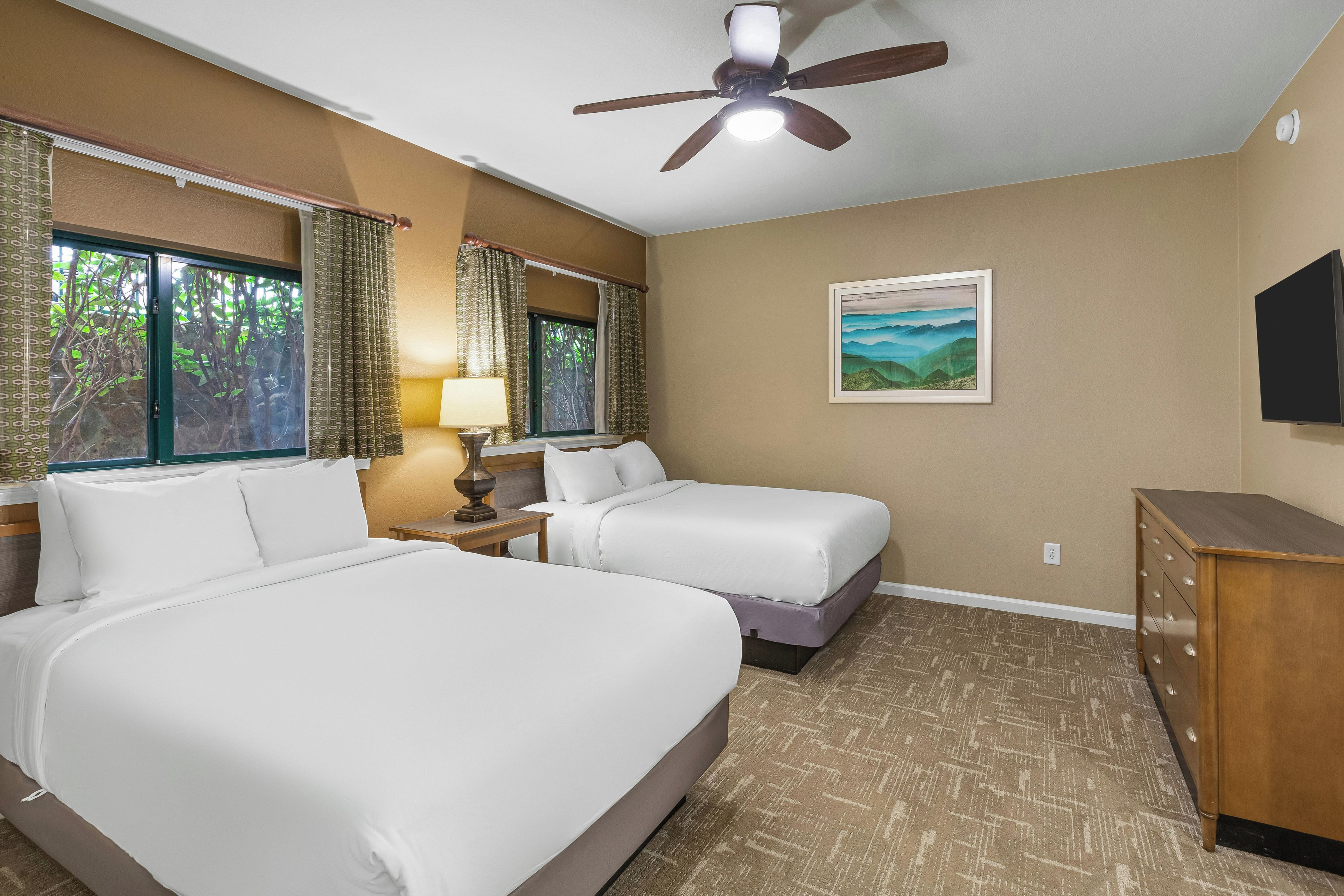 A hotel room with two beds, a ceiling fan, a painting, and a TV.