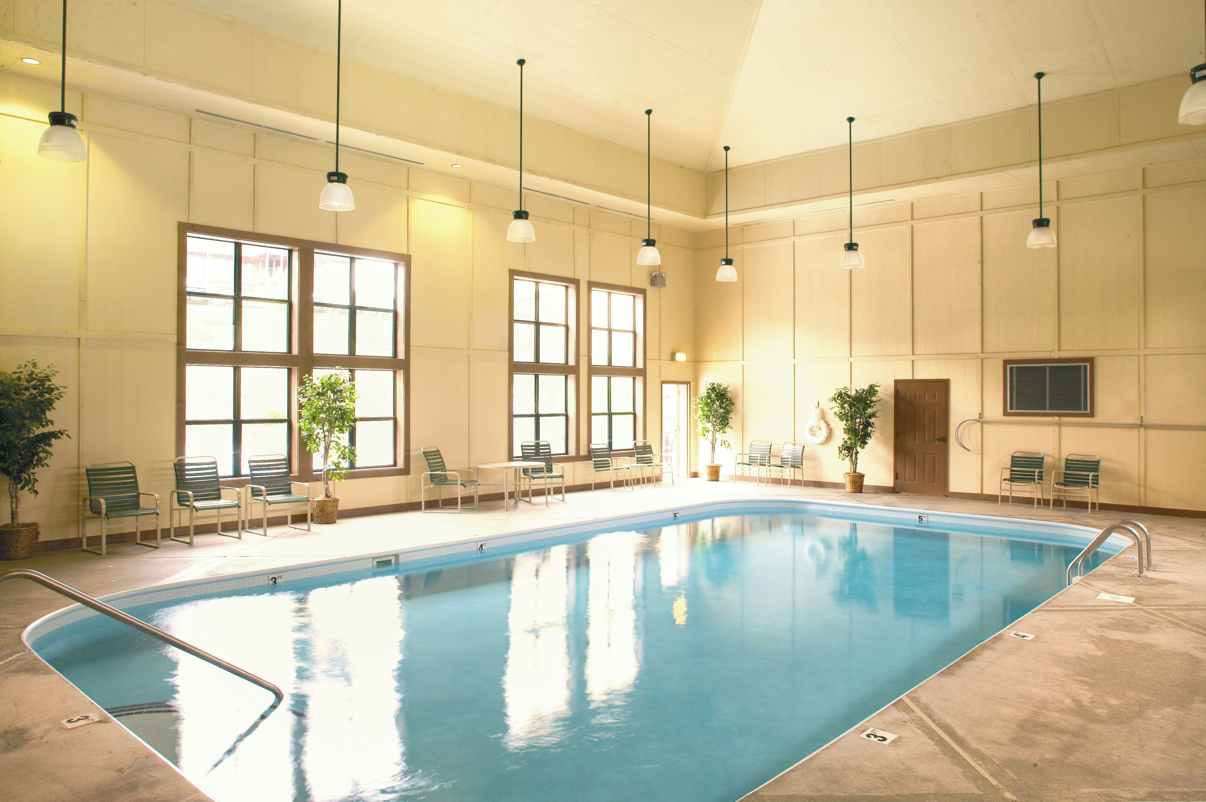 Une piscine intérieure à l’eau claire, entourée de chaises et de plantes en pot.