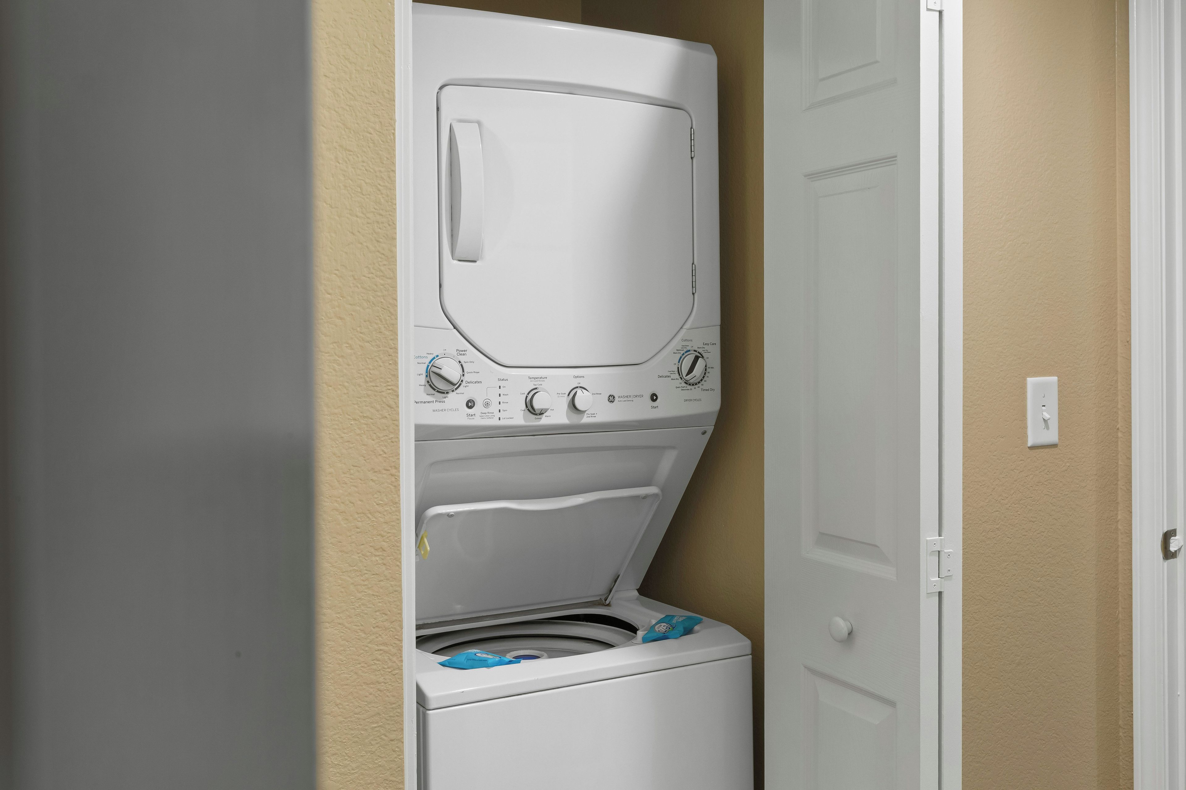 A compact washer and dryer unit installed in a corner of a room with beige walls.