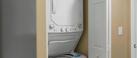 A compact washer and dryer unit installed in a corner of a room with beige walls.