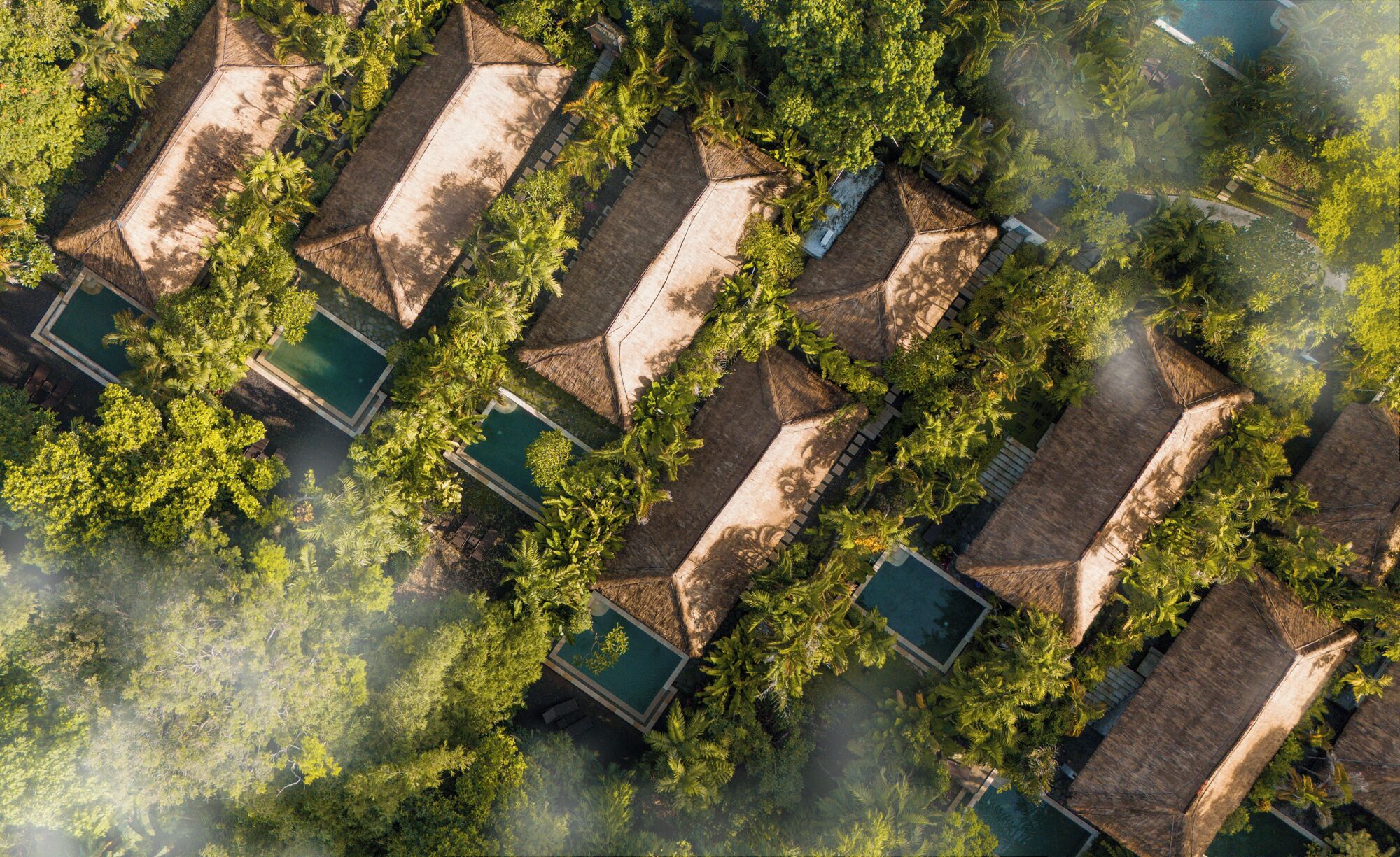 An aerial view of a resort with multiple bungalow-style accommodations, each with a private pool and surrounded by lush greenery.