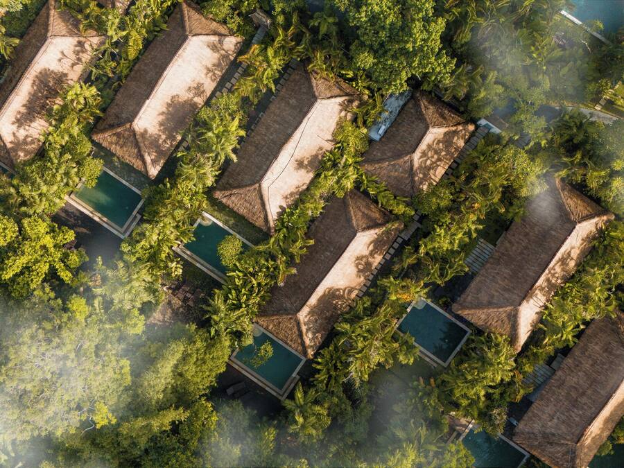 An aerial view of a resort with multiple bungalow-style accommodations, each with a private pool and surrounded by lush greenery.