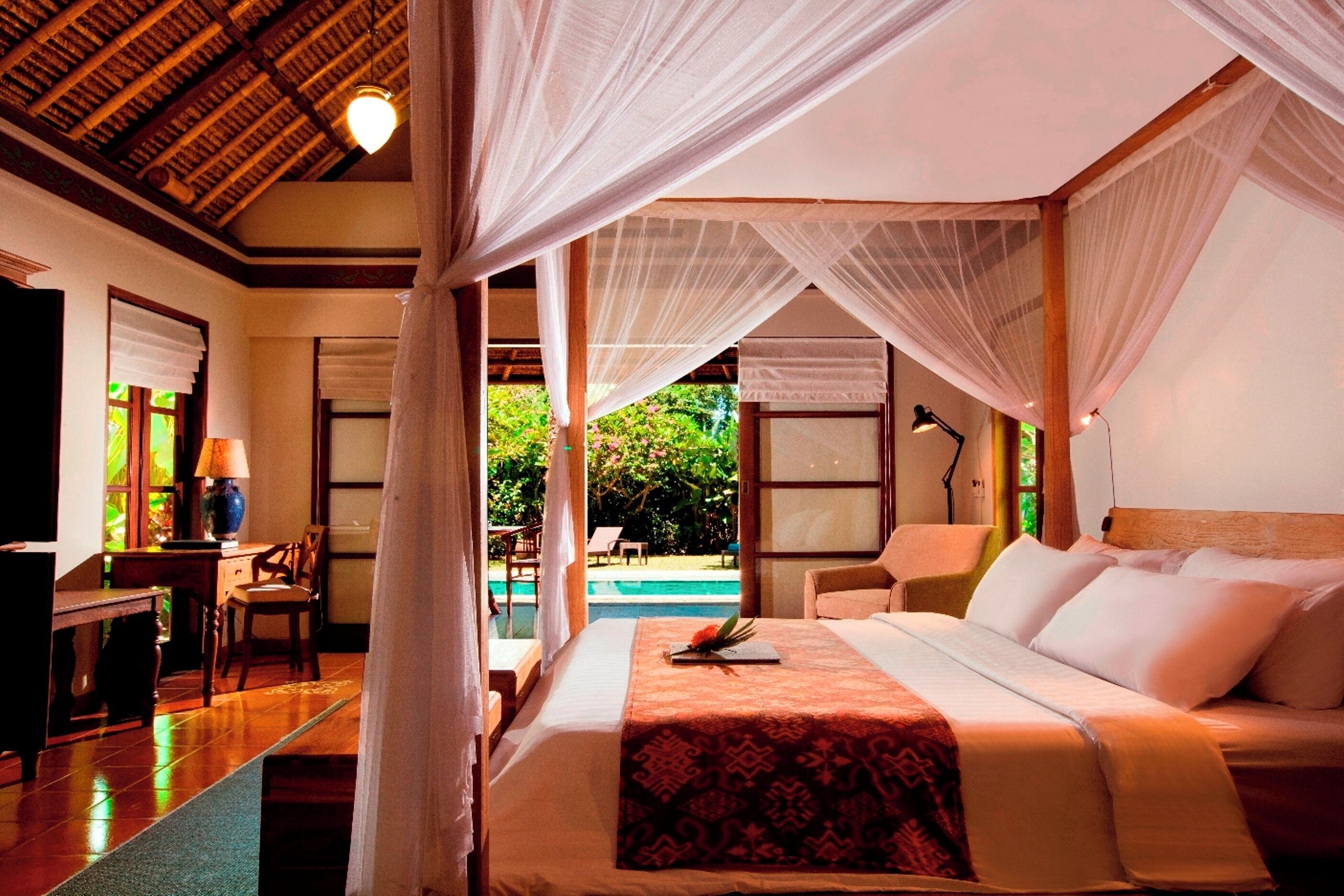 Un dormitorio con cama, escritorio, silla y vista a una piscina al aire libre.