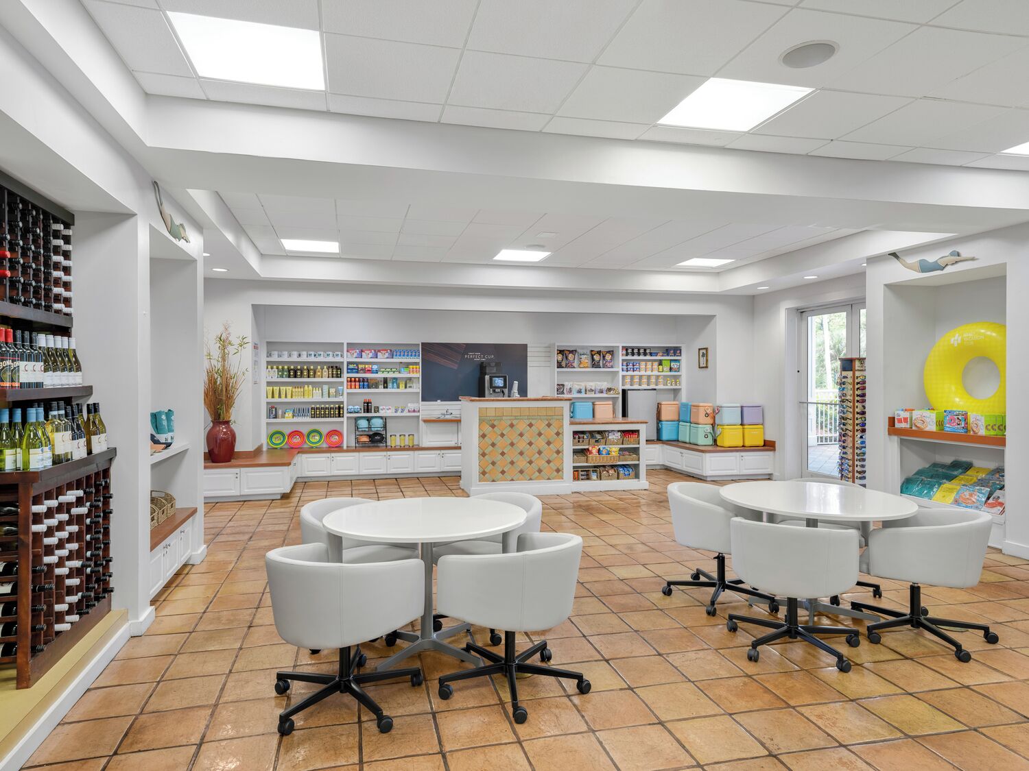A modern interior with white walls, tiled flooring, and multiple white tables and chairs.